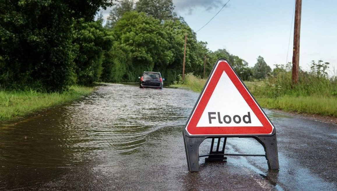 Essential Safety Tips for Flooded Roads | Warrington Van Hire | Central Warrington Van Hire | Call 01925 396 222 A van driving cautiously through shallow water on flooded roads, creating a small bow wave to protect the engine while maintaining a steady, slow speed.