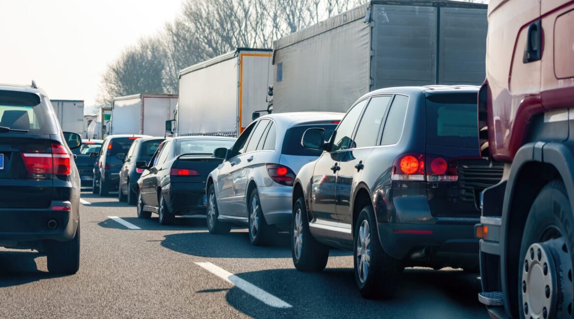 A white hire van in heavy traffic on a busy UK road, maintaining a safe following distance from the vehicle in front during rush hour congestion.